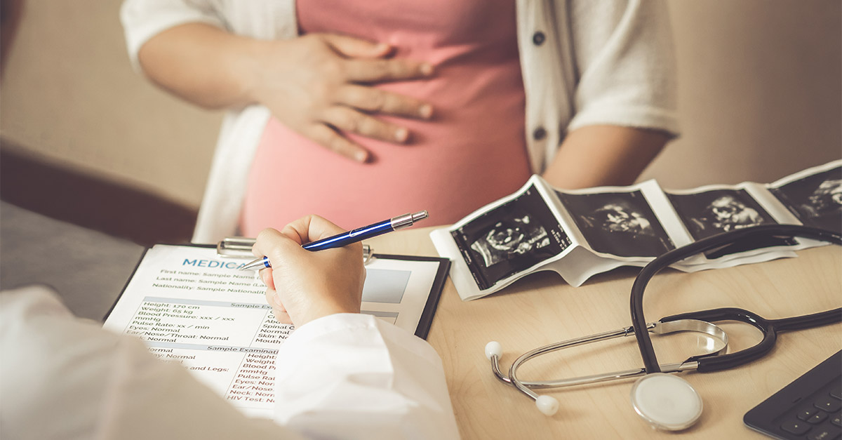 Doctor reviewing medical records and ultrasound images with pregnant patient, representing OB/GYN workforce and physician compensation challenges.
