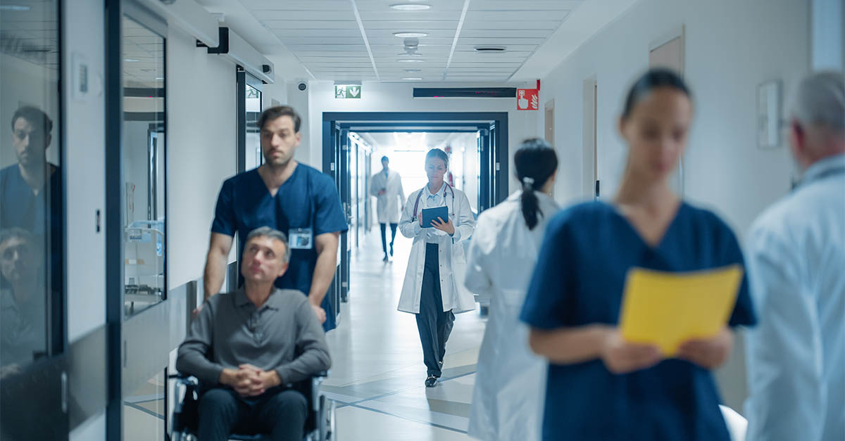 Busy hospital corridor with patients being transported and physicians reviewing clinical charts during daily operations