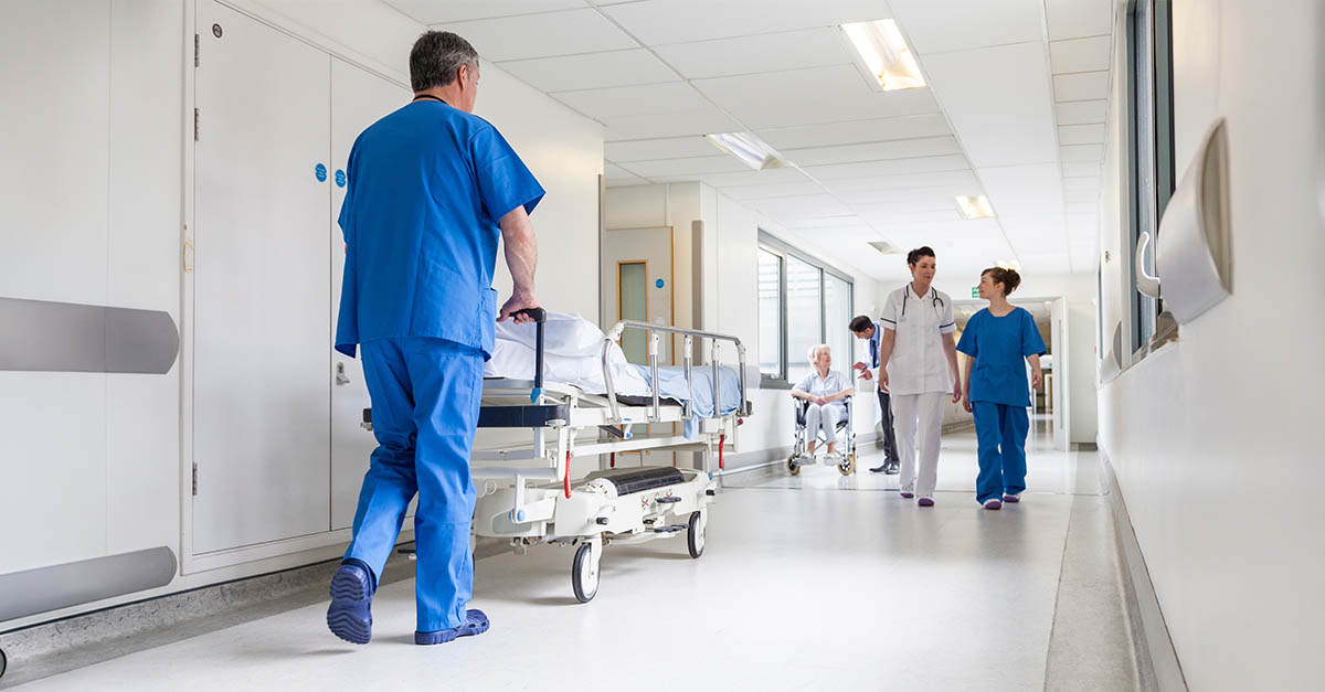 Healthcare staff transporting a patient through a hospital hallway, representing patient flow, transitions of care, and academic medical center operations