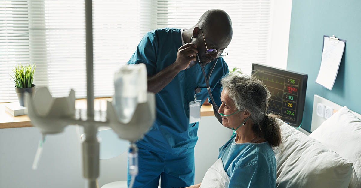Clinician using a stethoscope to examine an older hospital patient receiving oxygen