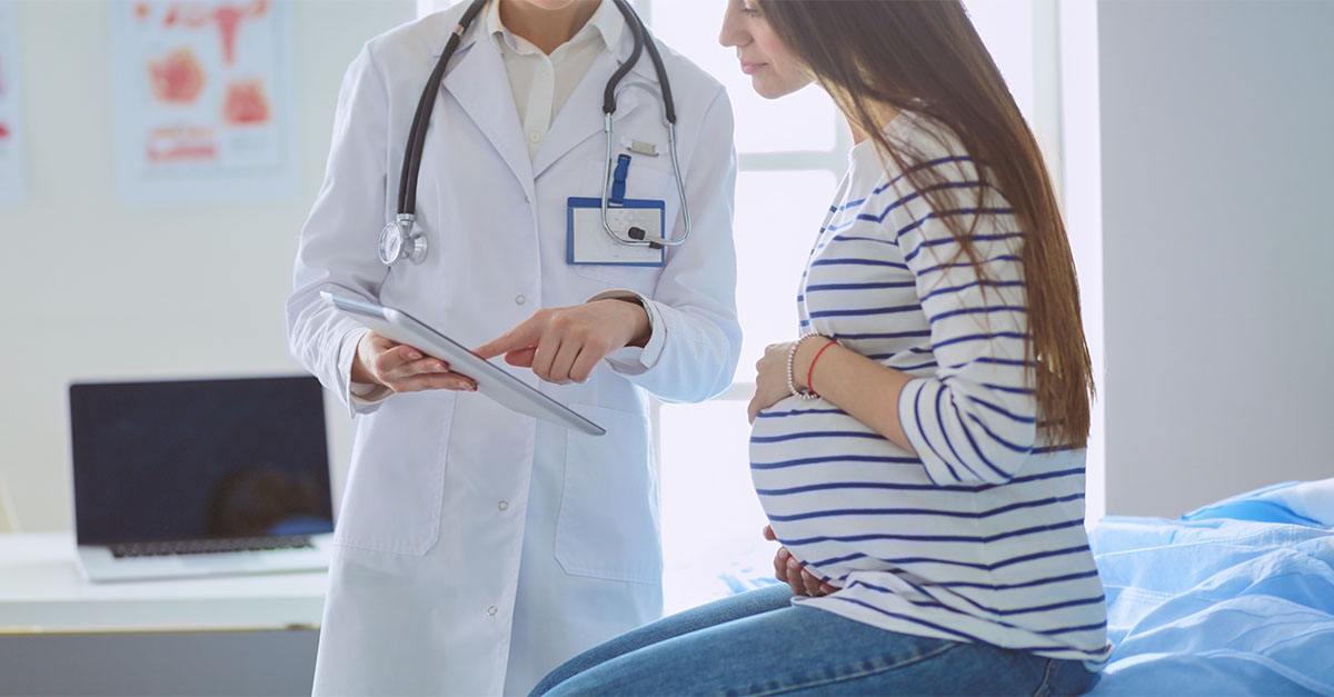 Clinician reviewing information on a tablet with a pregnant patient